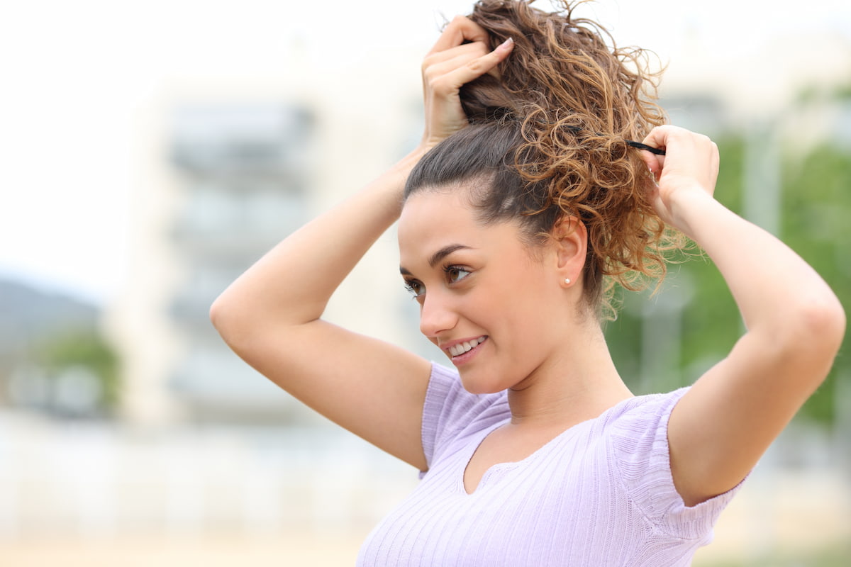 Woman standing outside and putting her curly hair in ponytail Woman standing outside and putting her curly hair in ponytail